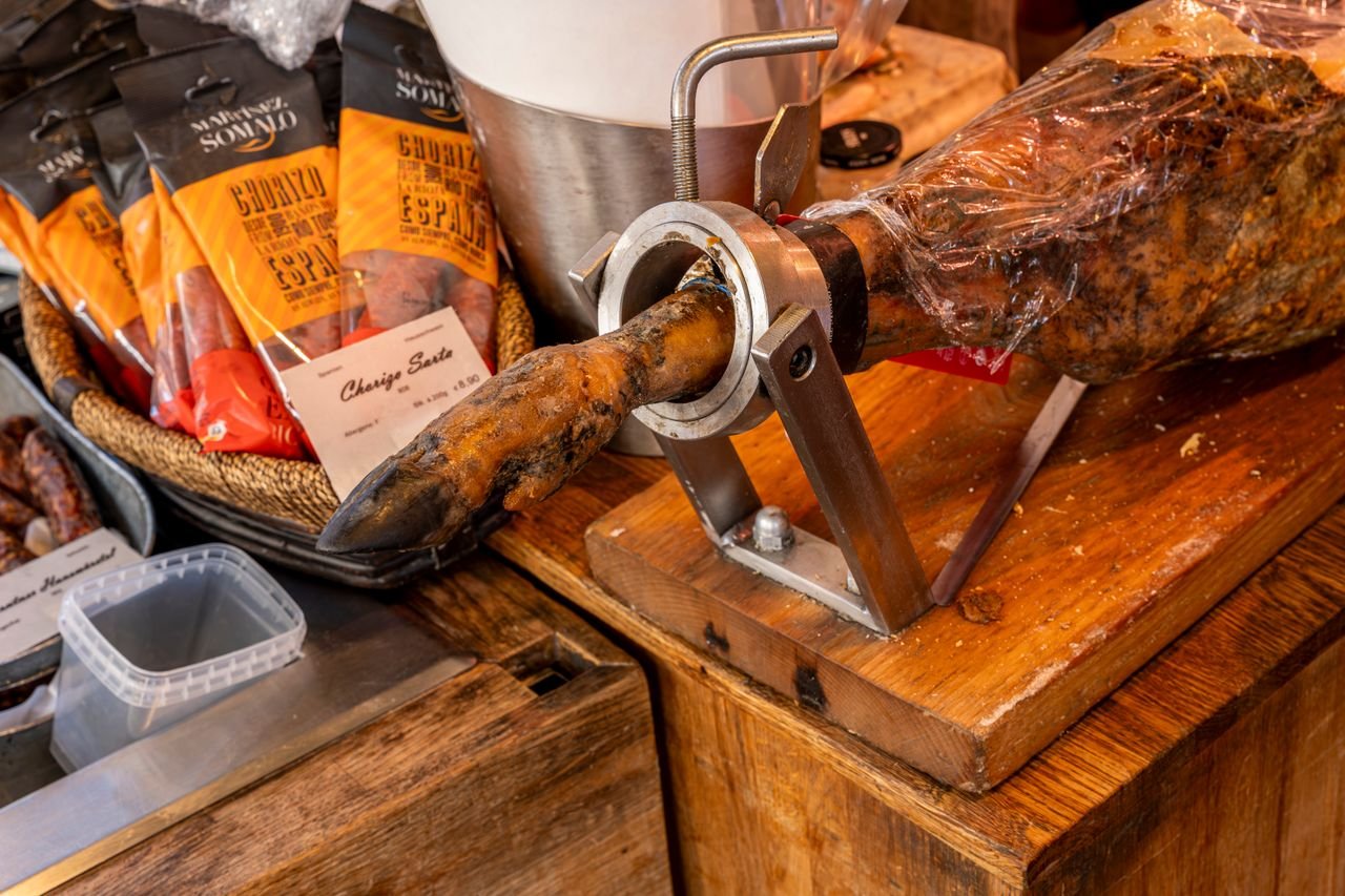 Close-up of cured meats including Spanish ham and chorizo in a gourmet shop display.